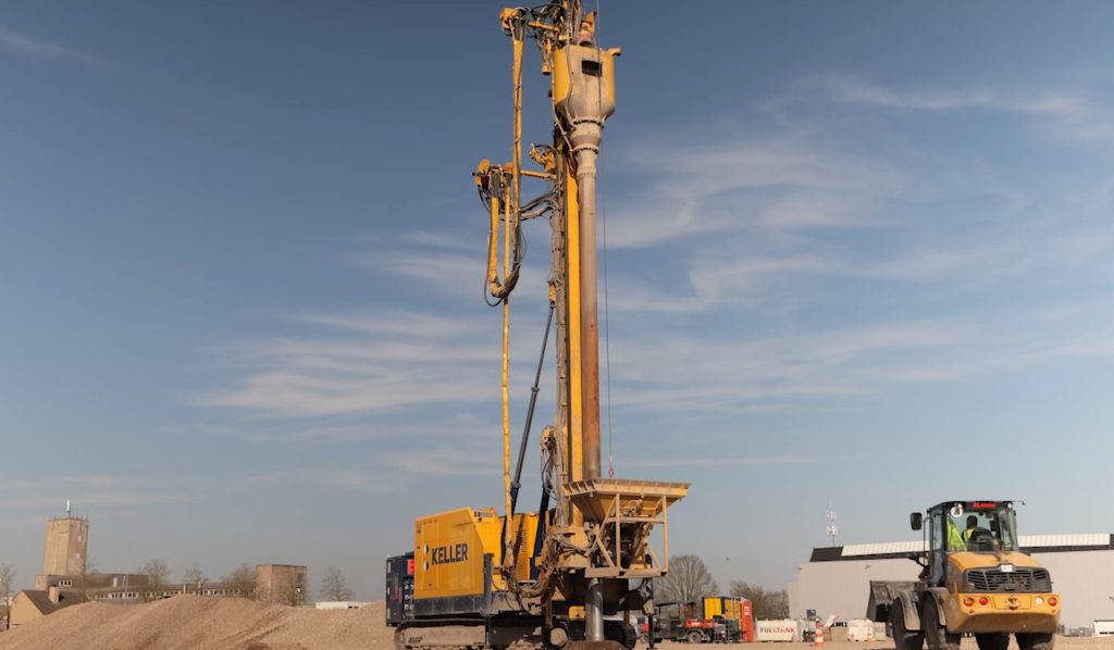 Bouwplaats met grote gele boormachine en kraan.
