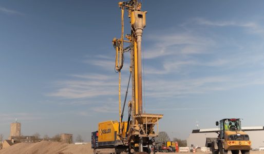Bouwplaats met grote gele boormachine en kraan.