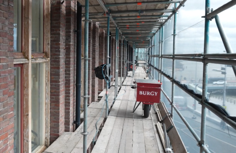 Bouwsteiger met kruiwagen en uitzicht op straat.