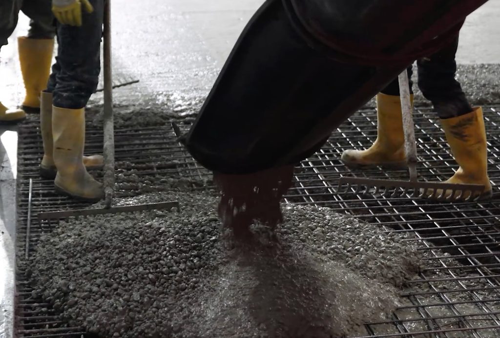 Bouwvakkers storten beton op stalen rooster met laarzen.