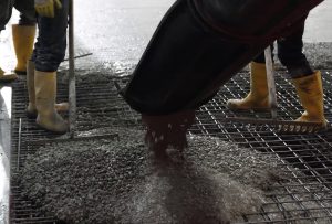 Bouwvakkers storten beton op stalen rooster met laarzen.