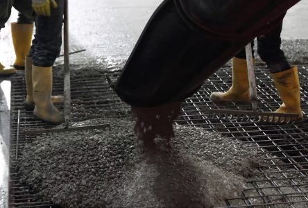 Bouwvakkers storten beton op stalen rooster met laarzen.