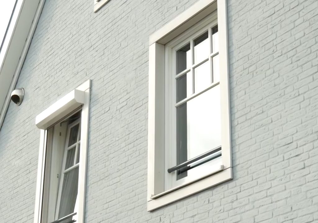 Grijze bakstenen muur met witte raamkozijnen.