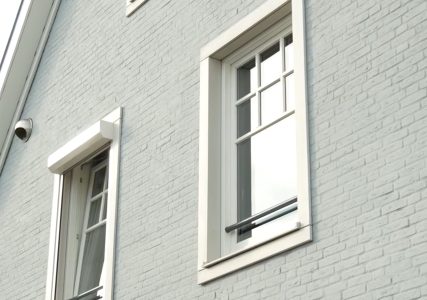 Grijze bakstenen muur met witte raamkozijnen.