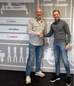 Twee mannen schudden handen voor bedrijfsmuur.