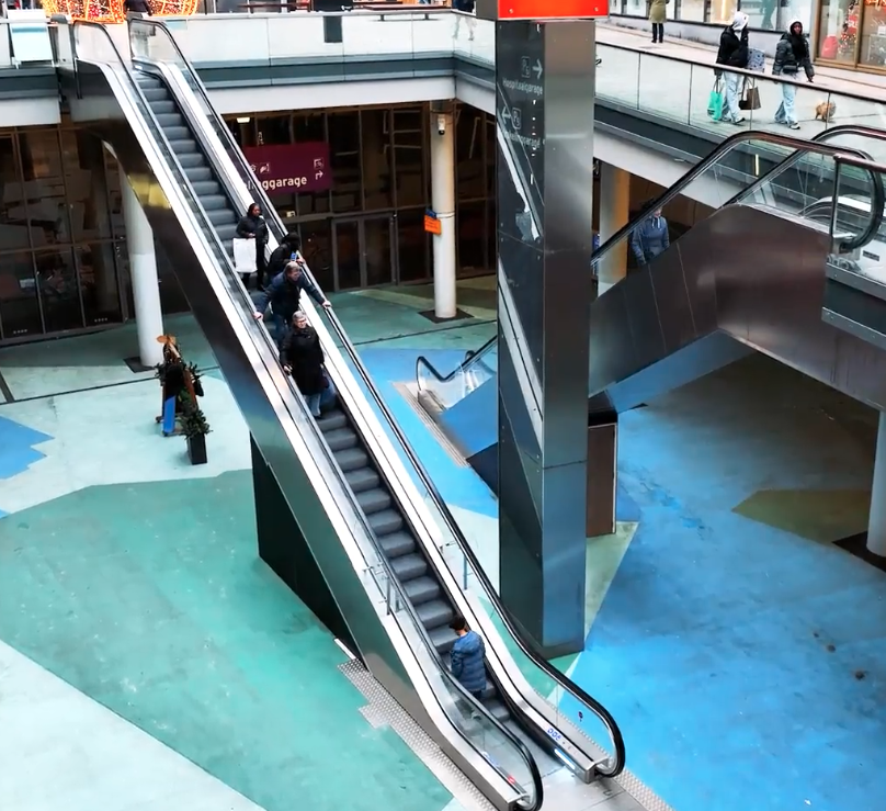 Winkelcentrum met roltrappen en wandelende mensen.