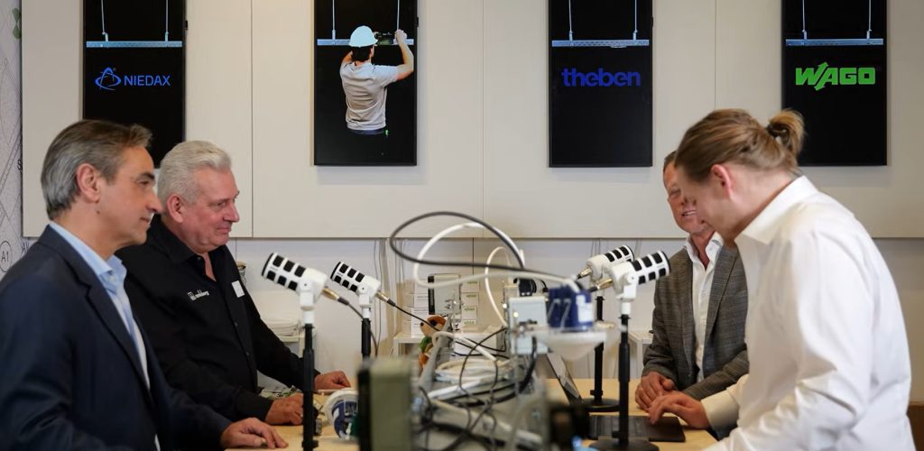 Mannen praten rond tafel met microfoons en apparatuur.