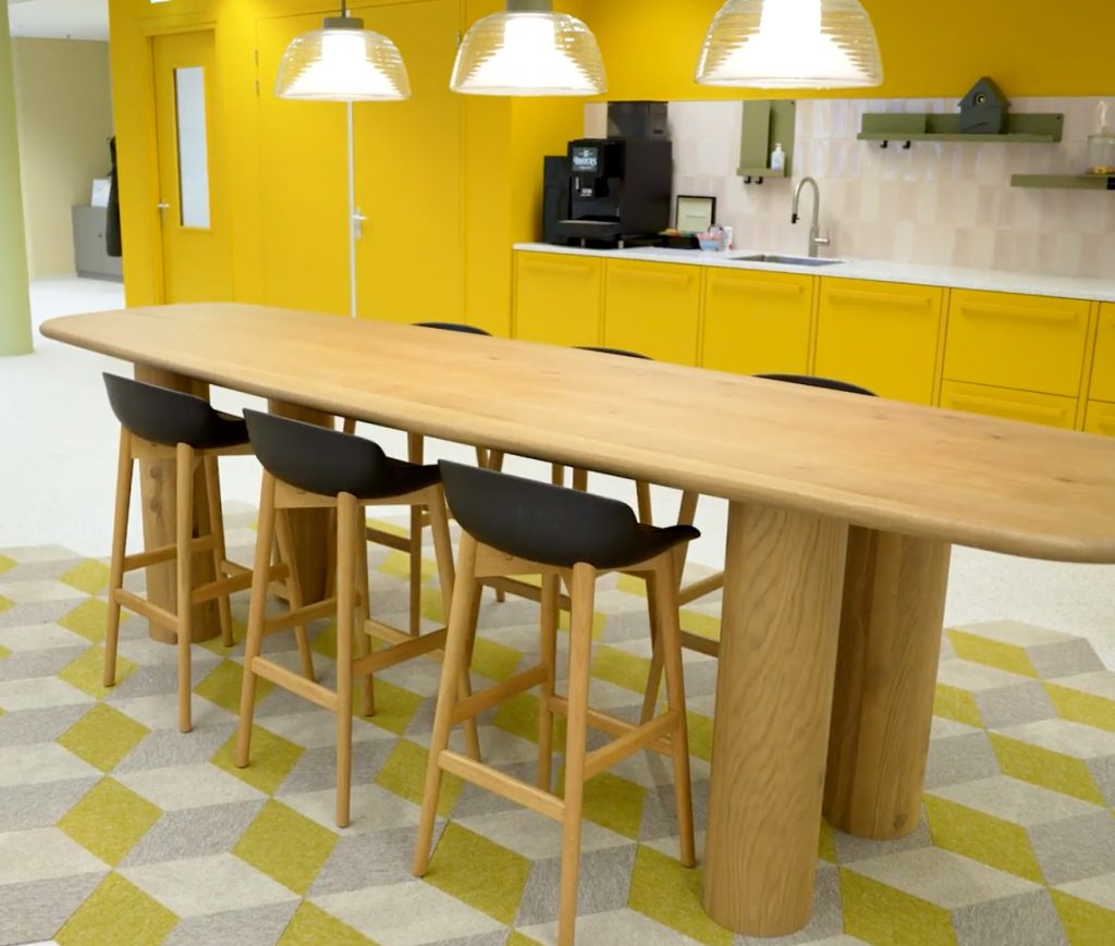 Gezellige kantine met houten tafel en gele kasten.