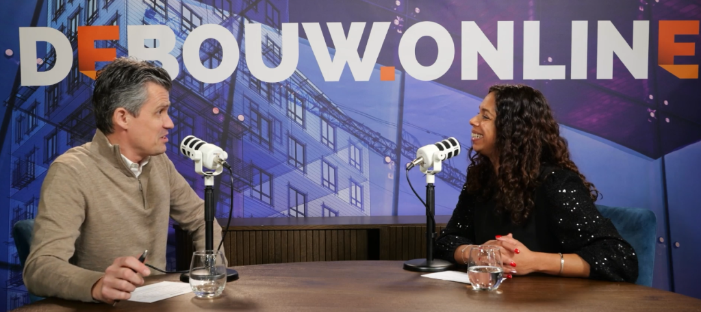 Twee mensen in gesprek bij microfoons in studio.